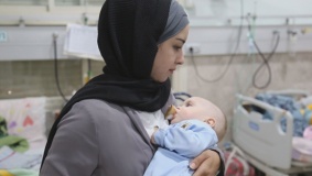 أم متطوعة ترعى رضيعاً غزياً في رحلة علاجه بالخليل