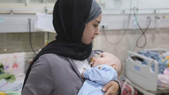أم متطوعة ترعى رضيعاً غزياً في رحلة علاجه بالخليل